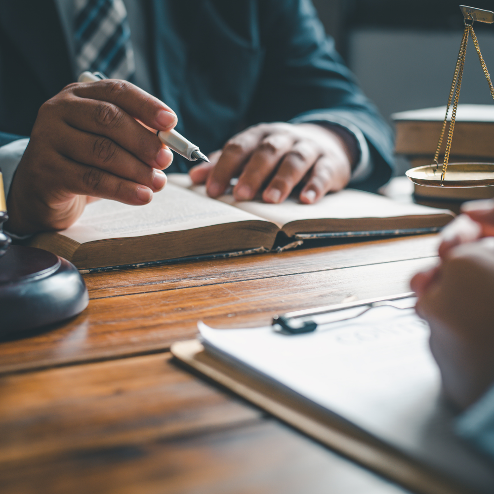 Two people in business attire, reviewing documents at a wooden desk; scales of justice and a gavel visible.