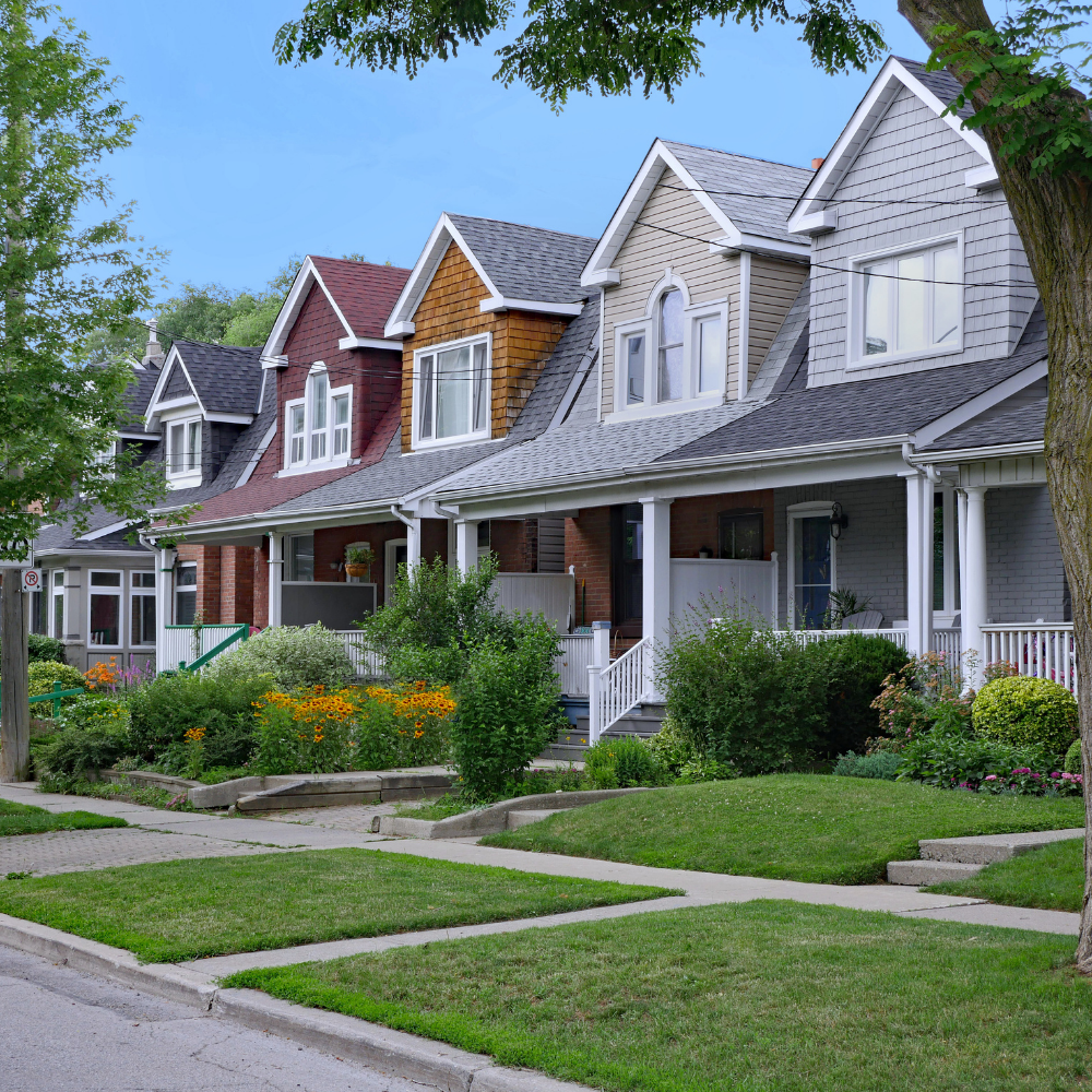 Row of colorful houses with front yards and sidewalks on a sunny day.