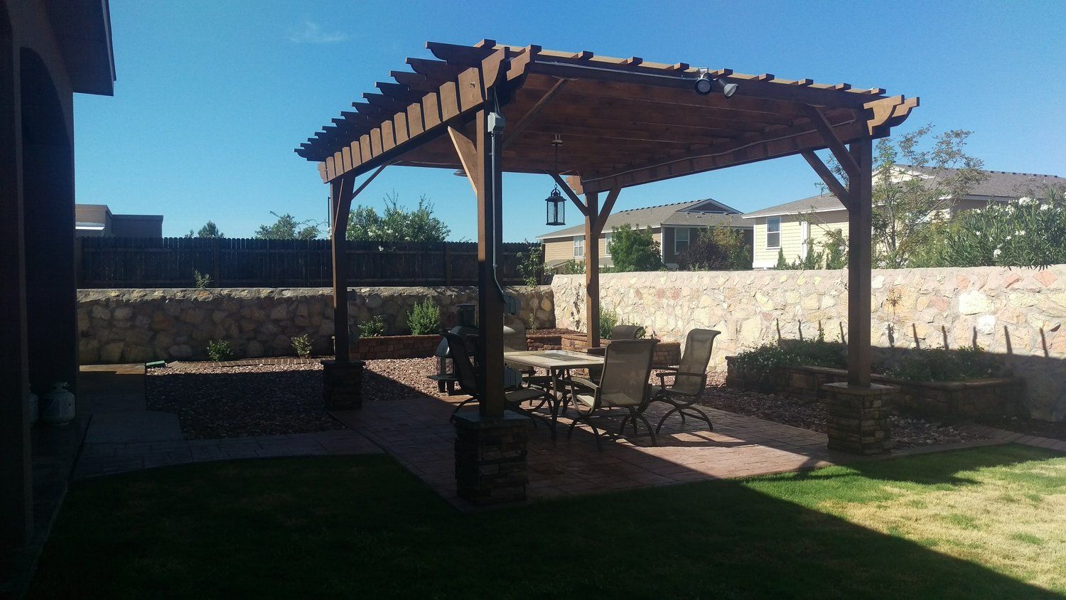 There is a pergola in the backyard with a table and chairs underneath it.