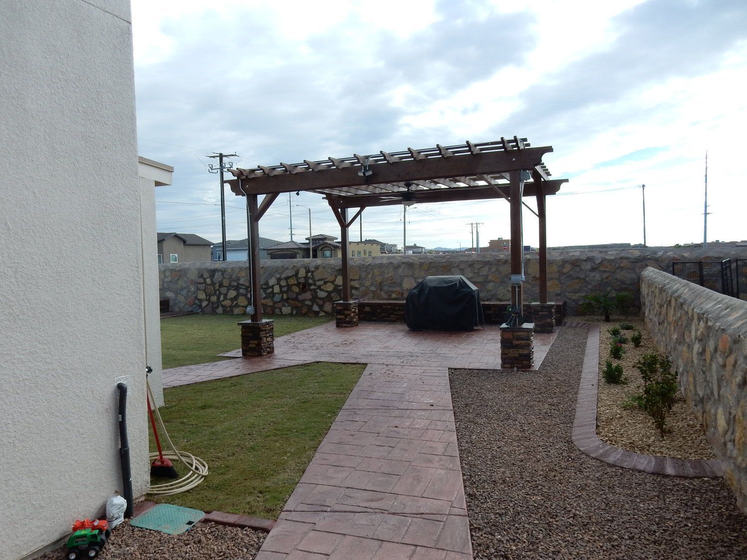 A brick walkway leading to a pergola in a backyard