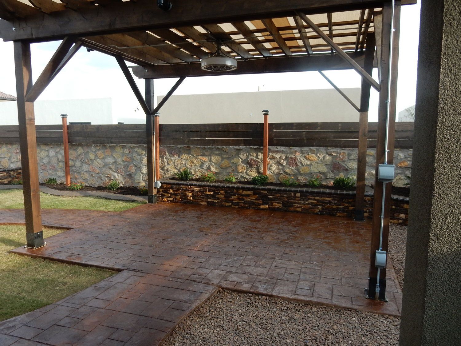 A patio with a wooden pergola and a brick walkway