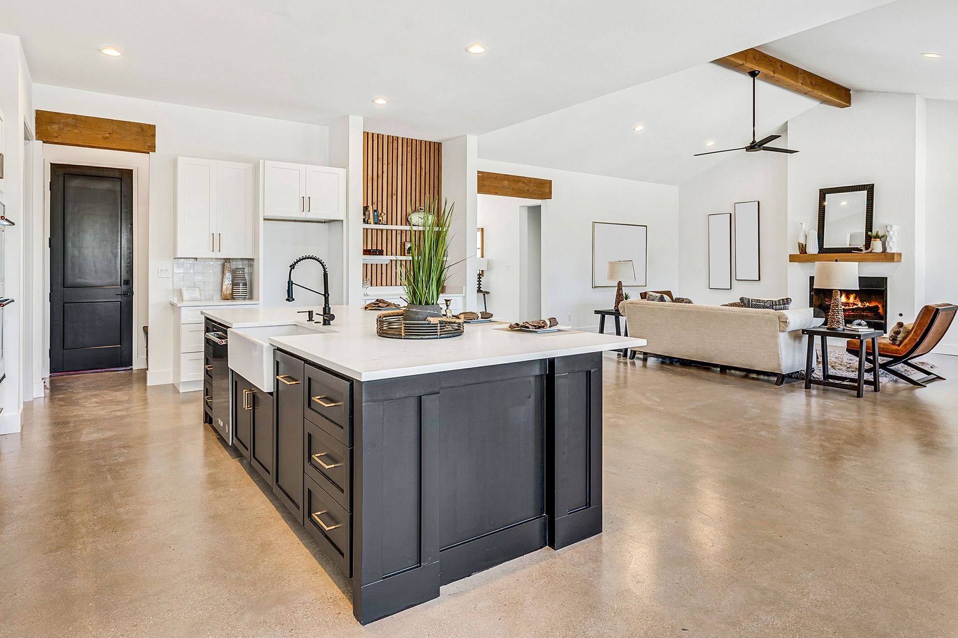 Modern open-concept kitchen with dark island, white countertops, and living room with fireplace.