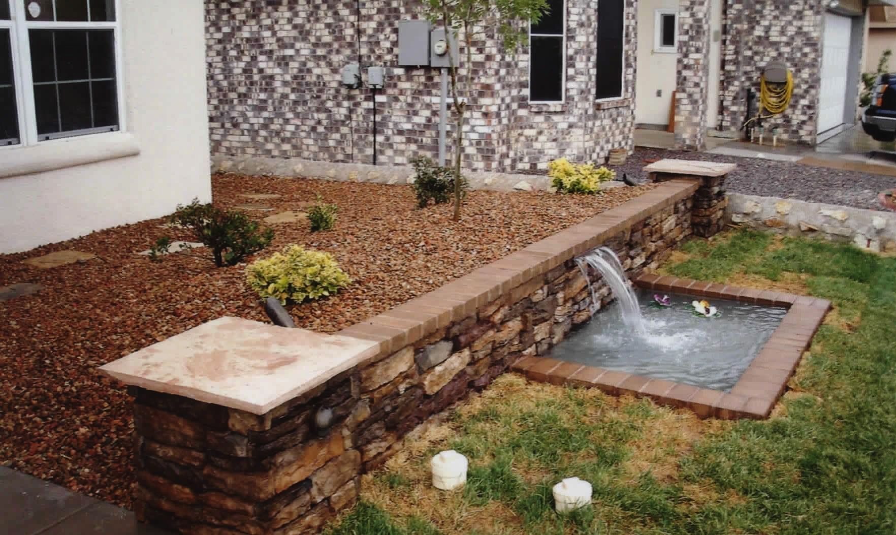 A stone wall with a water fountain in front of a house