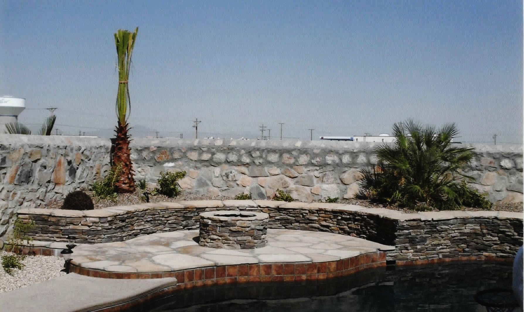 A stone wall surrounds a swimming pool with a palm tree in the foreground