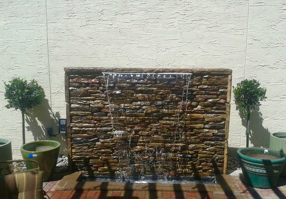 A waterfall is surrounded by potted plants and a brick wall