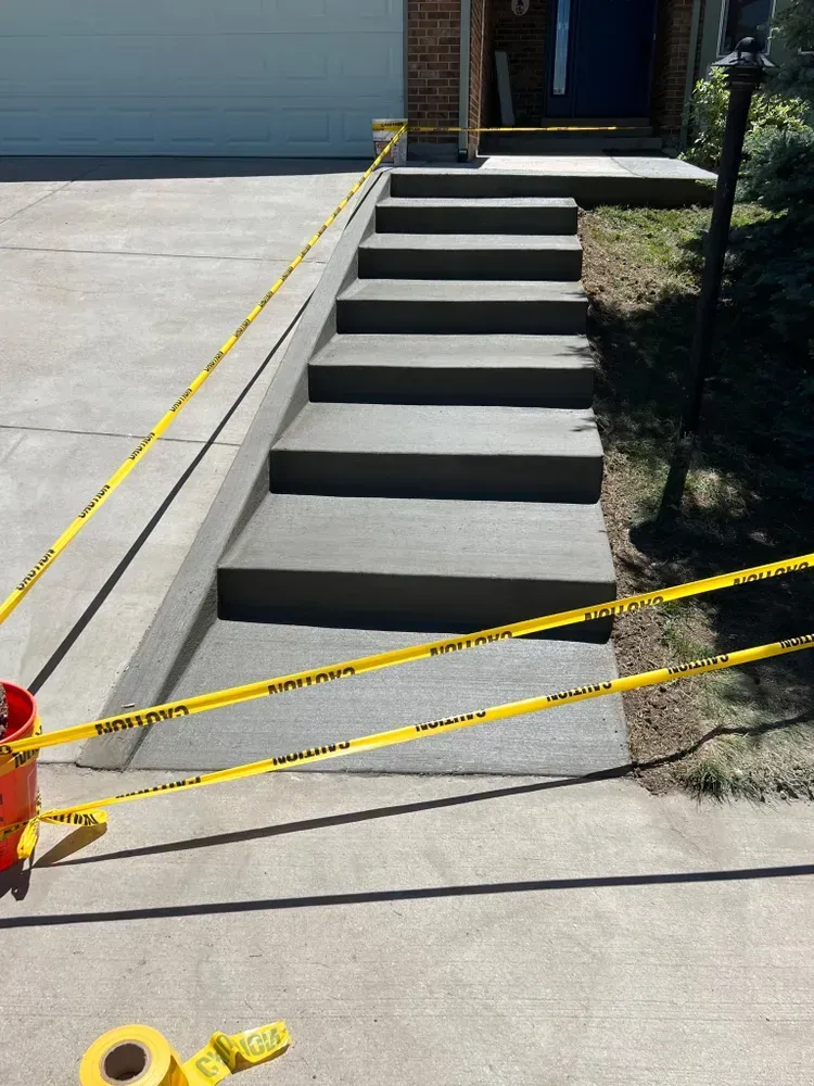 Newly poured concrete steps with caution tape, leading up to a house entrance.