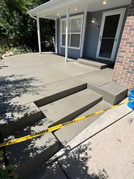 Newly poured concrete patio and steps with yellow caution tape, next to a house.