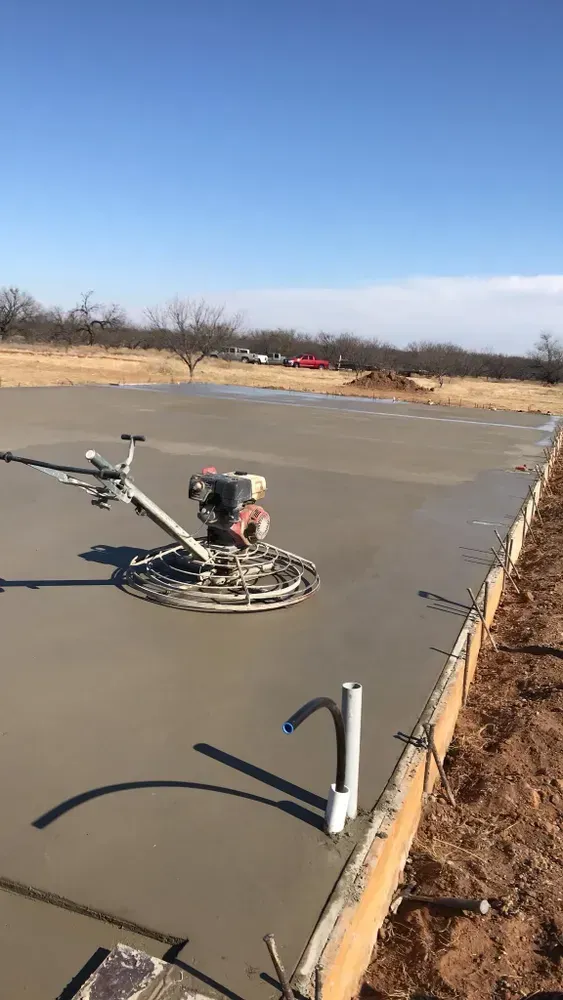 A concrete floor being finished with a power trowel, outdoors. Blue sky overhead.