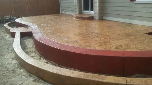 Tan and red stamped concrete patio with curved walls and steps, adjacent to a house.