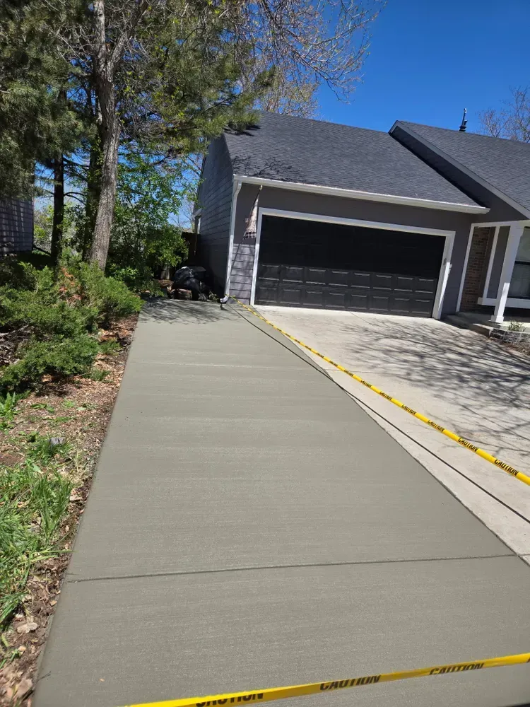 Freshly poured concrete driveway leading to a gray garage door, yellow caution tape bordering the driveway.