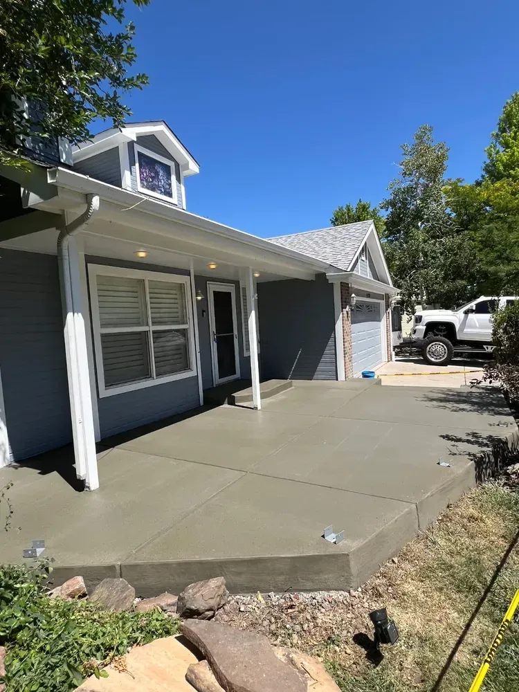 A freshly poured concrete patio in front of a house. Gray house, blue sky. White truck in the background.