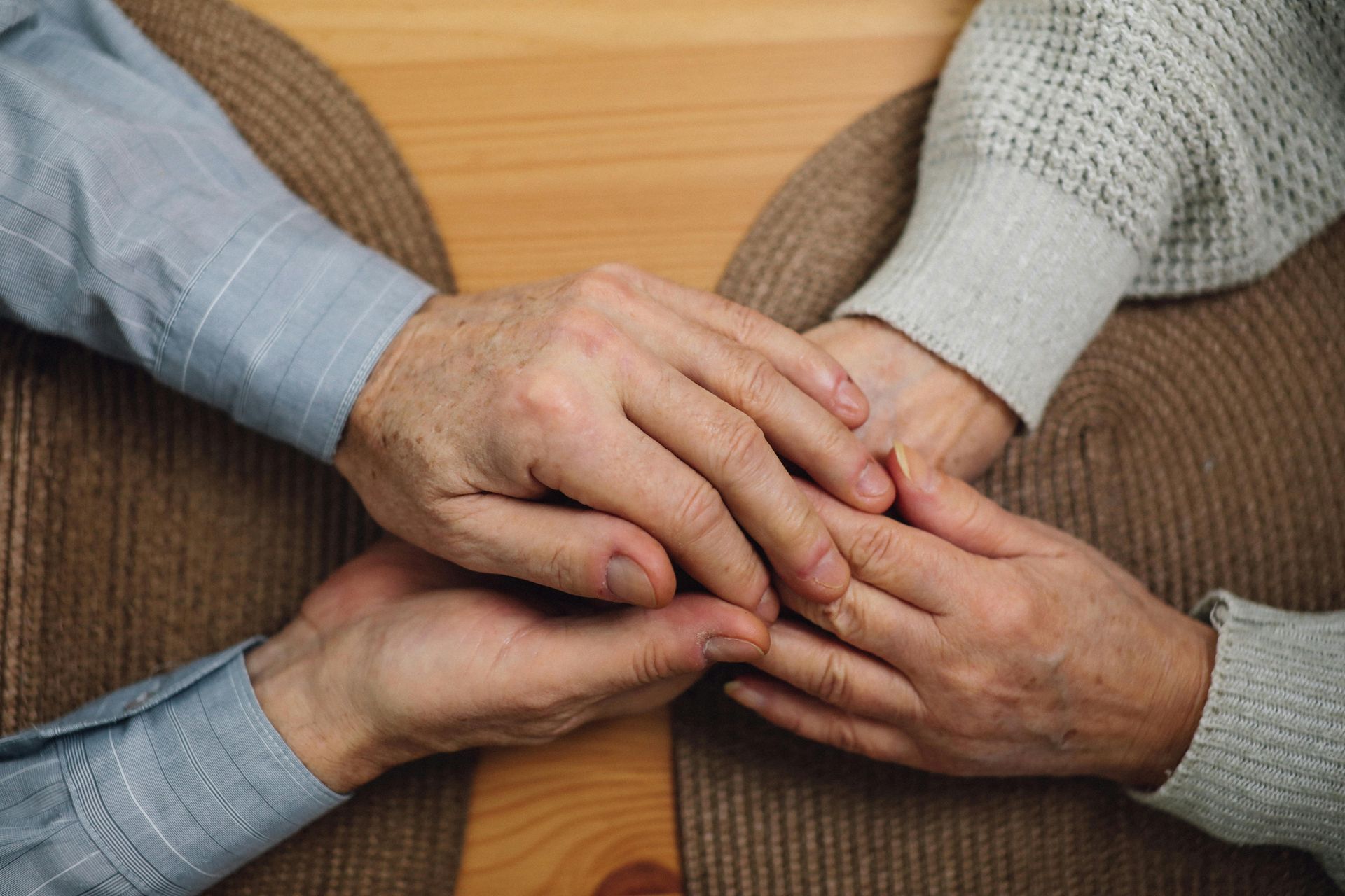 Two people's hands clasped together, showing support and comfort. One wears a blue shirt, the other a white sweater.