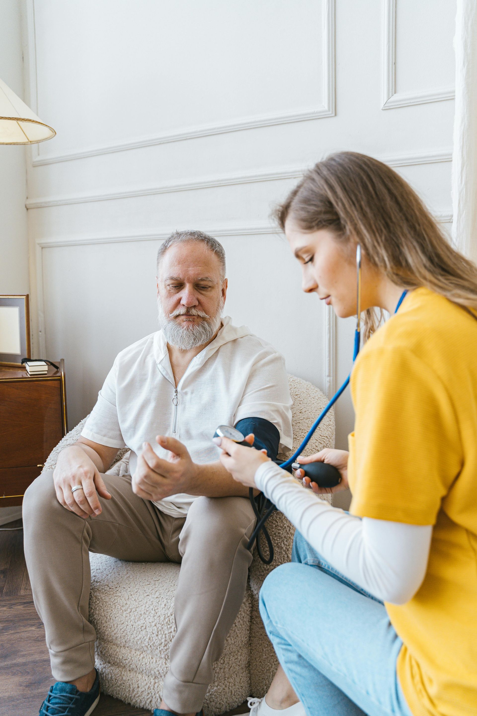 Woman in yellow shirt taking man's blood pressure indoors.