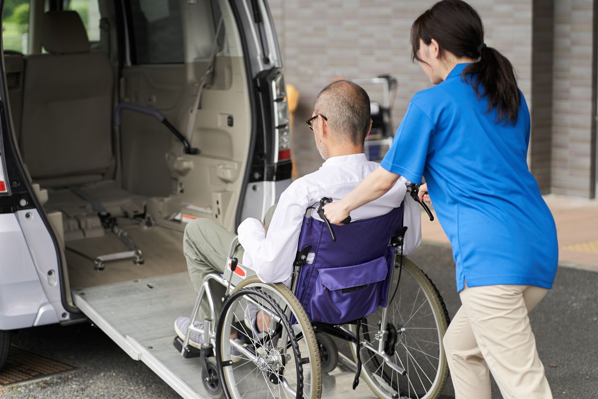 A person in a wheelchair is being assisted onto a wheelchair-accessible van by a caregiver.