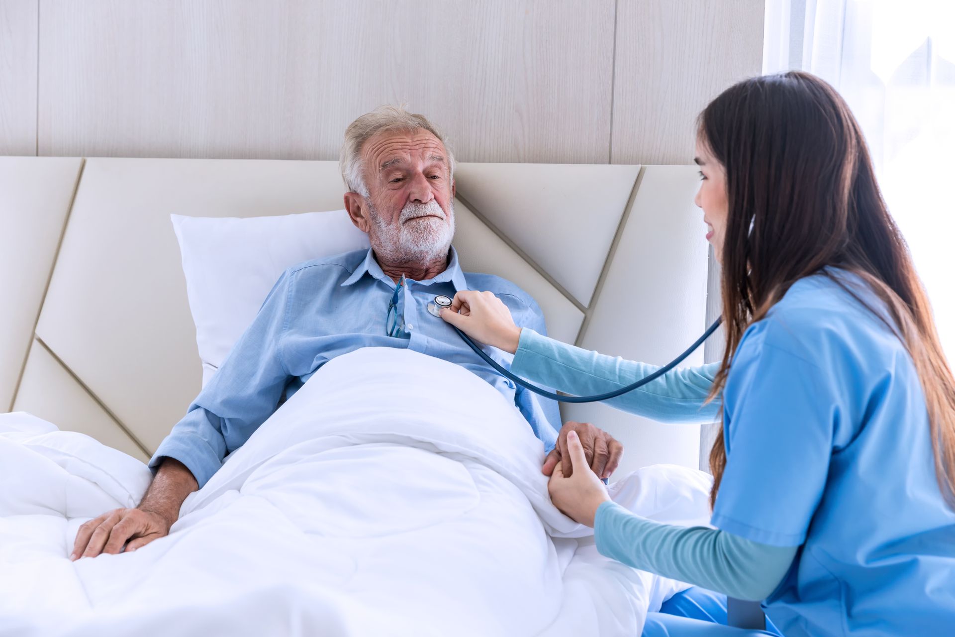 Nurse examining an older person's chest with a stethoscope in a bedroom. The person is lying in bed.