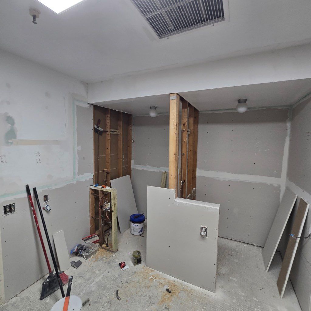 Bathroom renovation in progress, drywall installed, studs exposed. Tools and materials scattered.