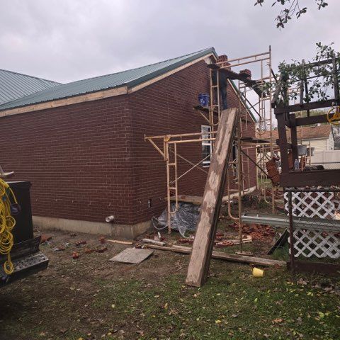 Brick building under construction, scaffolding, workers, brown brick, green roof, overcast sky.