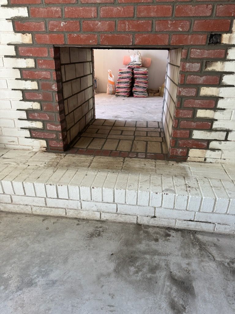 Fireplace with red and white brick detailing, open to another room with materials.