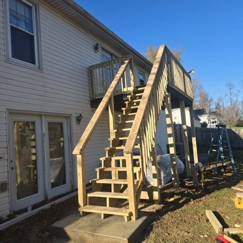 Wooden staircase leading to a second-story deck attached to a light-colored house. Clear blue sky overhead.
