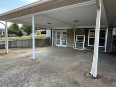 Carport with concrete floor. Two white support columns, white roof, and door. Windows on right.