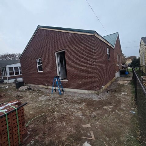 Red brick building under construction with open doorway and ladder.
