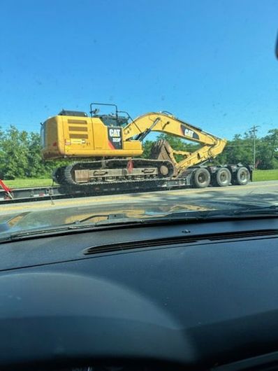 Yellow Caterpillar excavator on a trailer, ready for transport against a blue sky.