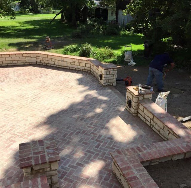 Brick patio under construction with brick and stone borders, worker near tools.