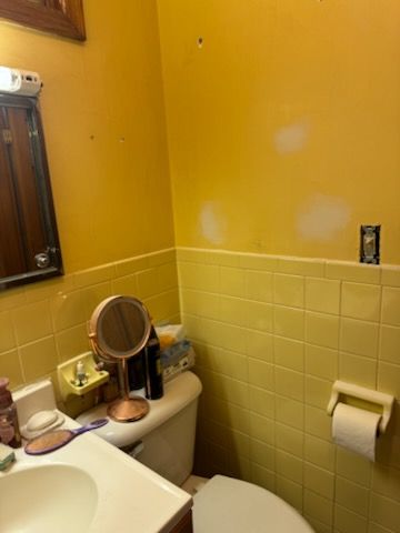 Yellow bathroom with tile, toilet, mirror, and paint patching on walls.