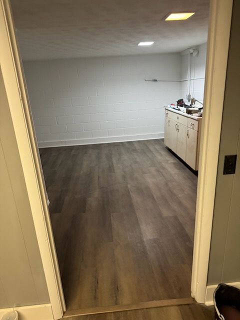 Room interior with wood-look flooring, white walls, and a cabinet visible in the back.