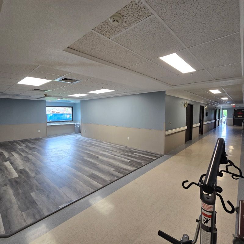 Interior hospital hallway with gray-blue walls, light wood-look floor, and a medical aid station in foreground.