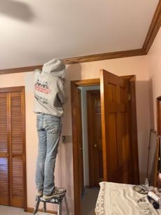 Person on a stool painting molding in a room with pink walls and wood trim.