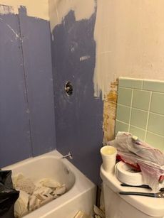 Bathroom undergoing renovation; blue walls, white tub, partially removed tiles, construction supplies.