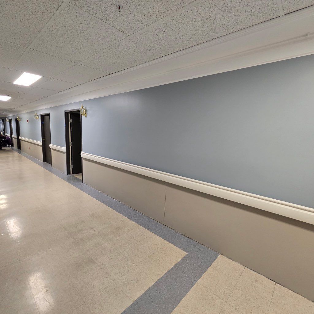 Hallway with doors, light blue wall, beige baseboard, and ceiling with fluorescent lights.