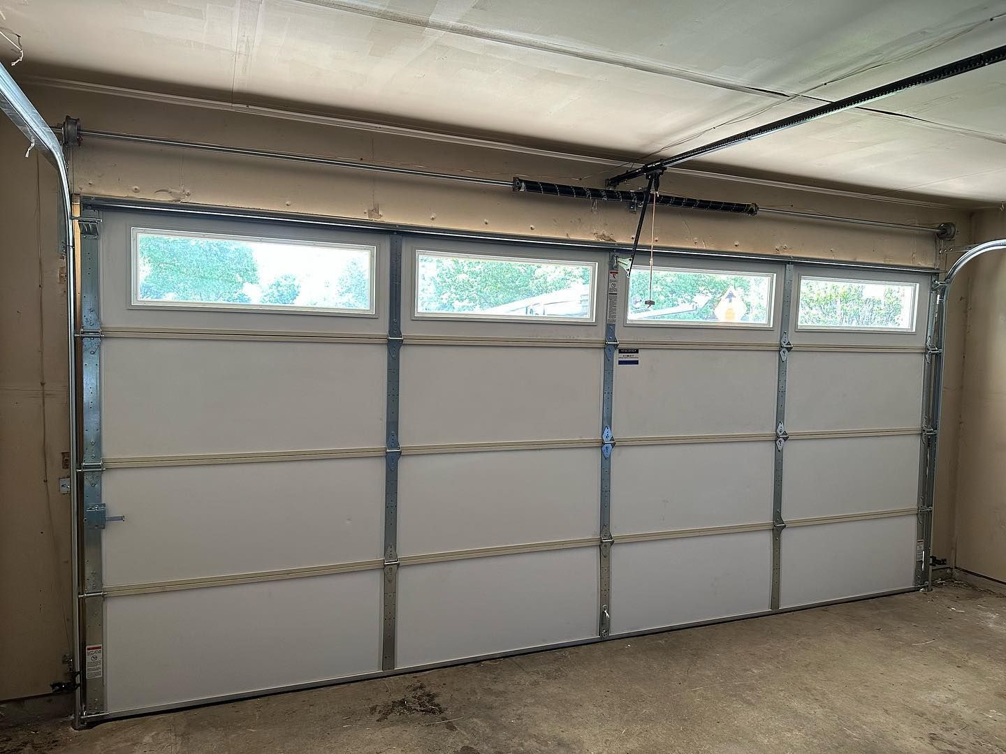 A white garage door with three windows is open in a garage.