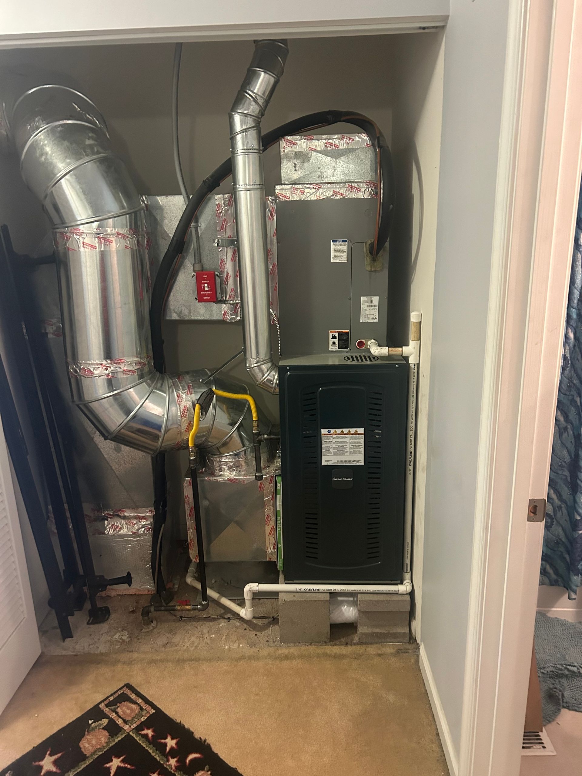 A room with a furnace , ducts , pipes and a rug.