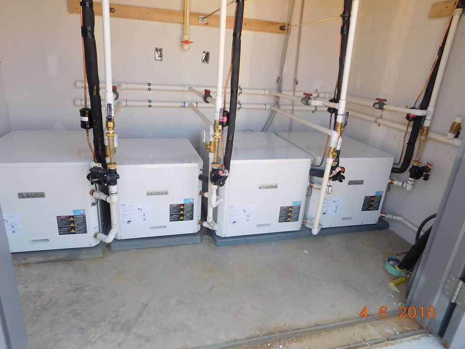 Three water heaters are lined up in a room with pipes.