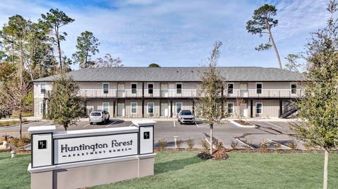 Huntington Forest apartment building, white sign on green lawn, parked cars in front.
