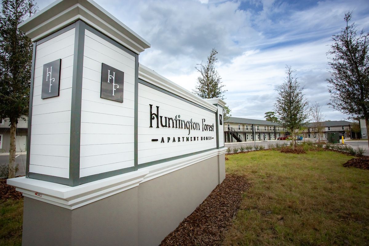Sign for Huntingdon Green Apartments, with building in the background, under cloudy sky.