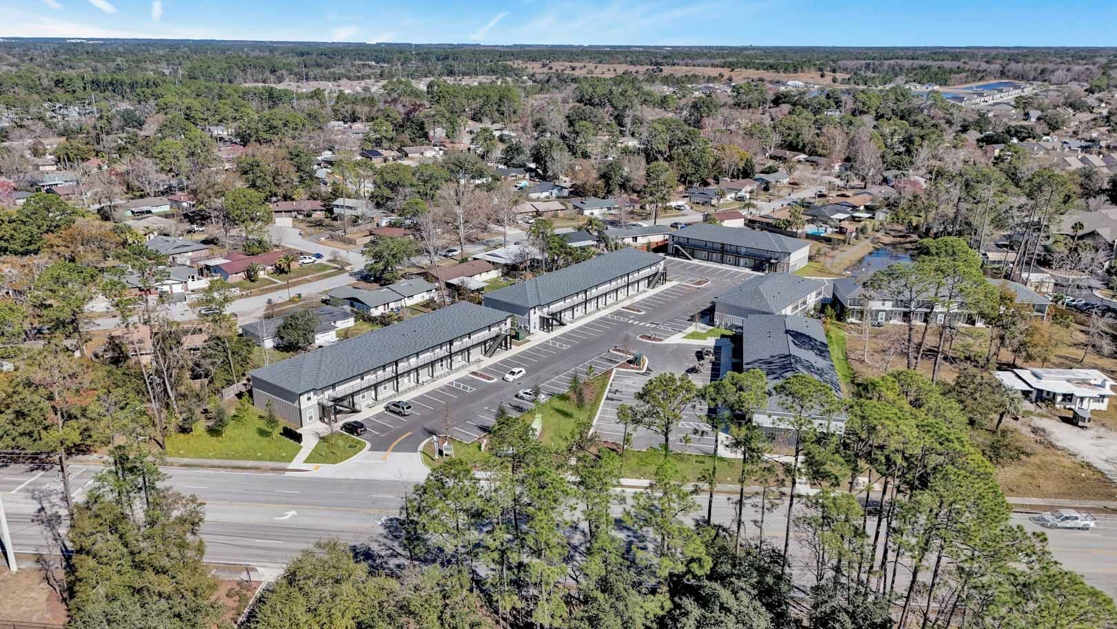 Aerial view of apartment complex with parking, trees, and residential neighborhood.