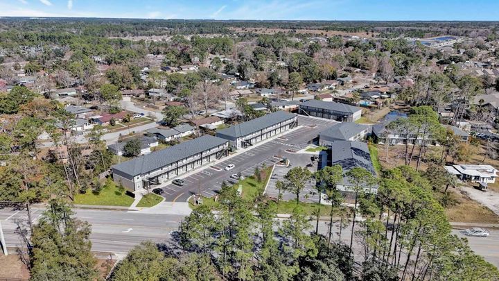 Aerial view of apartment complex with parking, trees, and residential neighborhood.