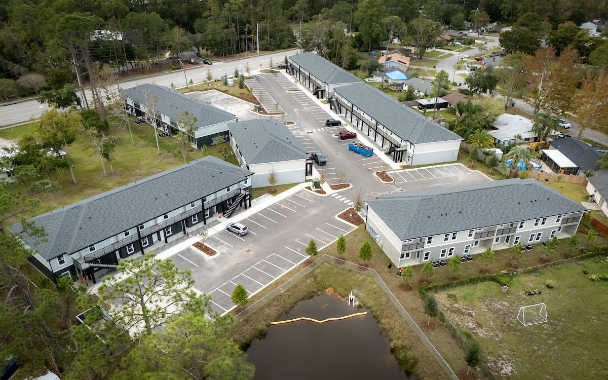 Aerial view of multi-unit apartment complex with gray roofs, light-colored walls, and parking.