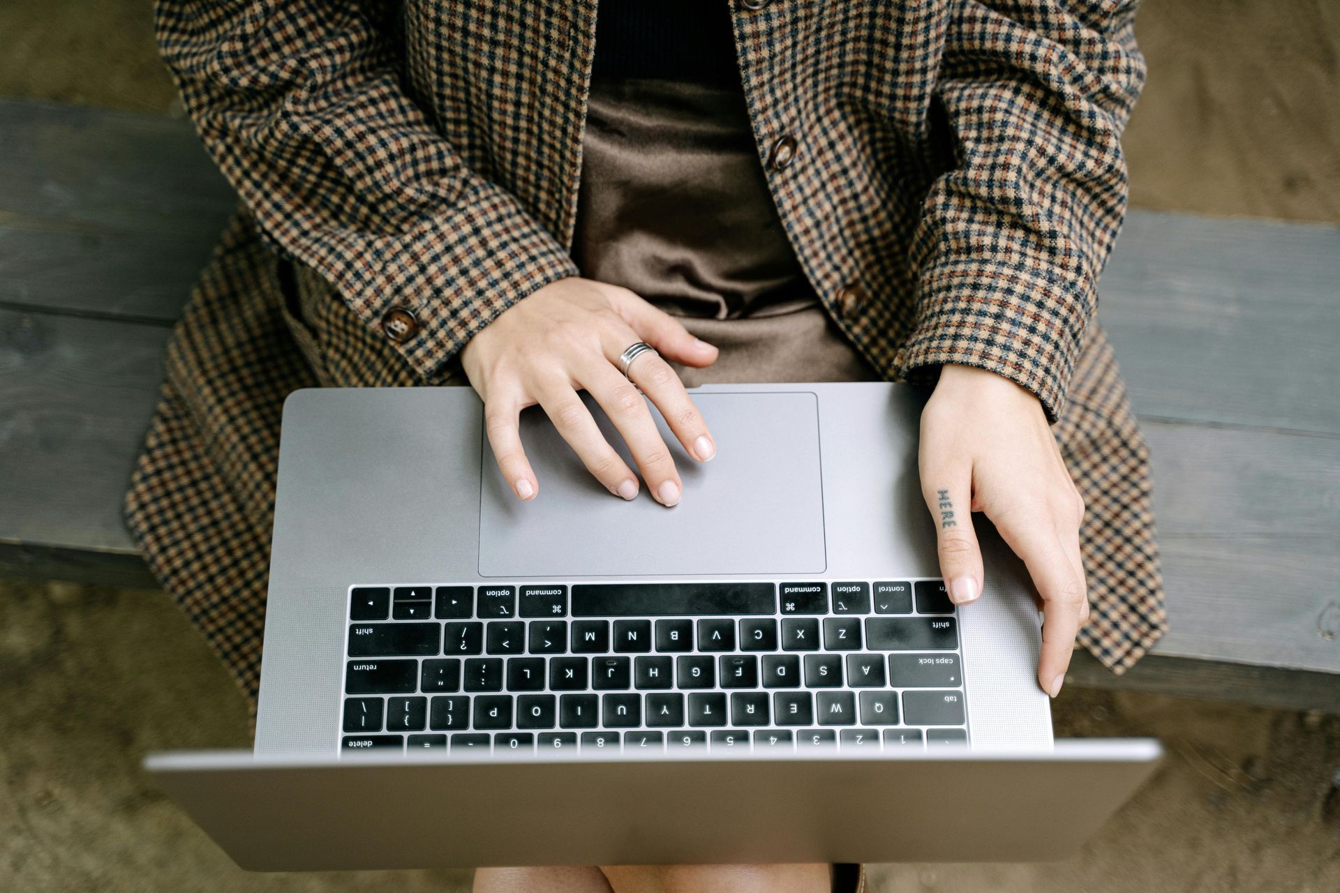 Person typing on a laptop with a brown plaid jacket and satin skirt.