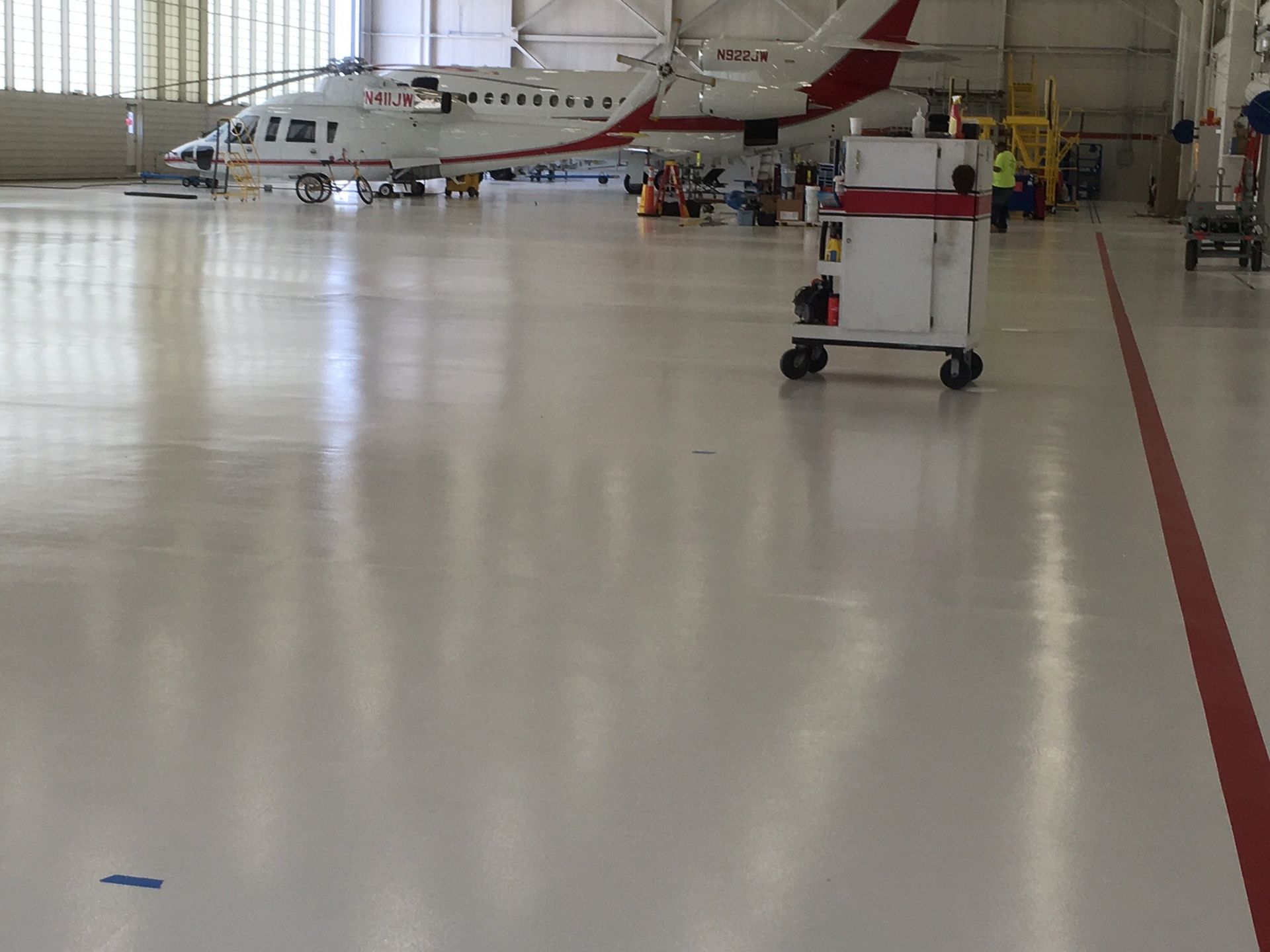 Shiny white hangar floor with an airplane, utility cart, and red line.