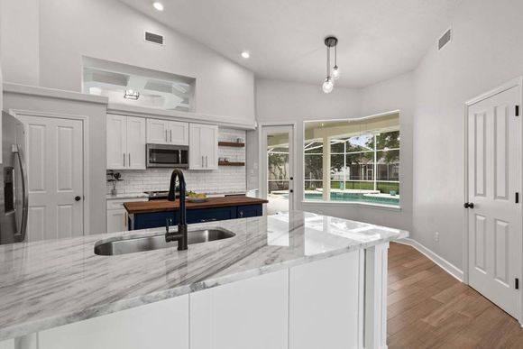 A kitchen with white cabinets , granite counter tops , a sink , and a large window.