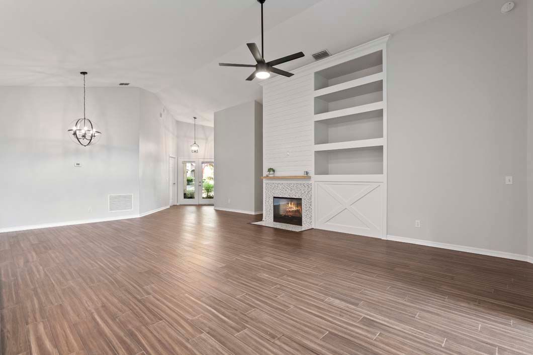 An empty living room with hardwood floors , a fireplace and a ceiling fan.