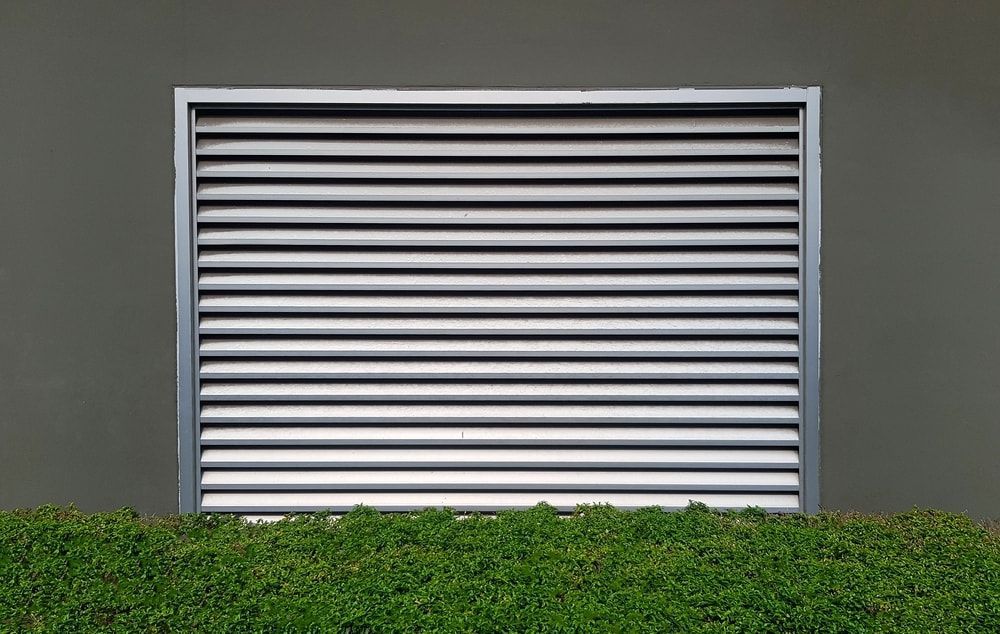 A Metal Shutter on the Side of a Building Next to a Hedge — Tully Blinds in Tully, QLD