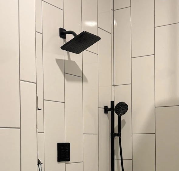 Modern matte black shower head and handheld shower wand installed against white vertical subway tile.