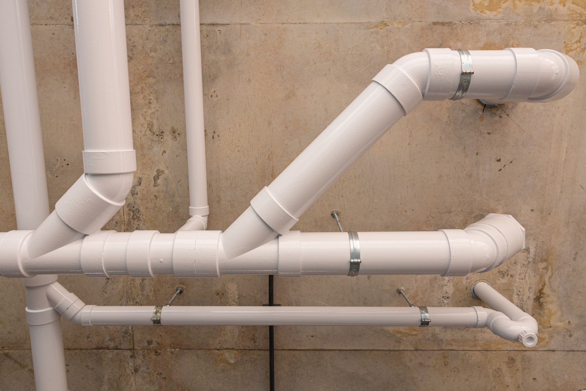 A network of white PVC pipes mounted to a concrete ceiling, joined by elbows and Y-fittings.
