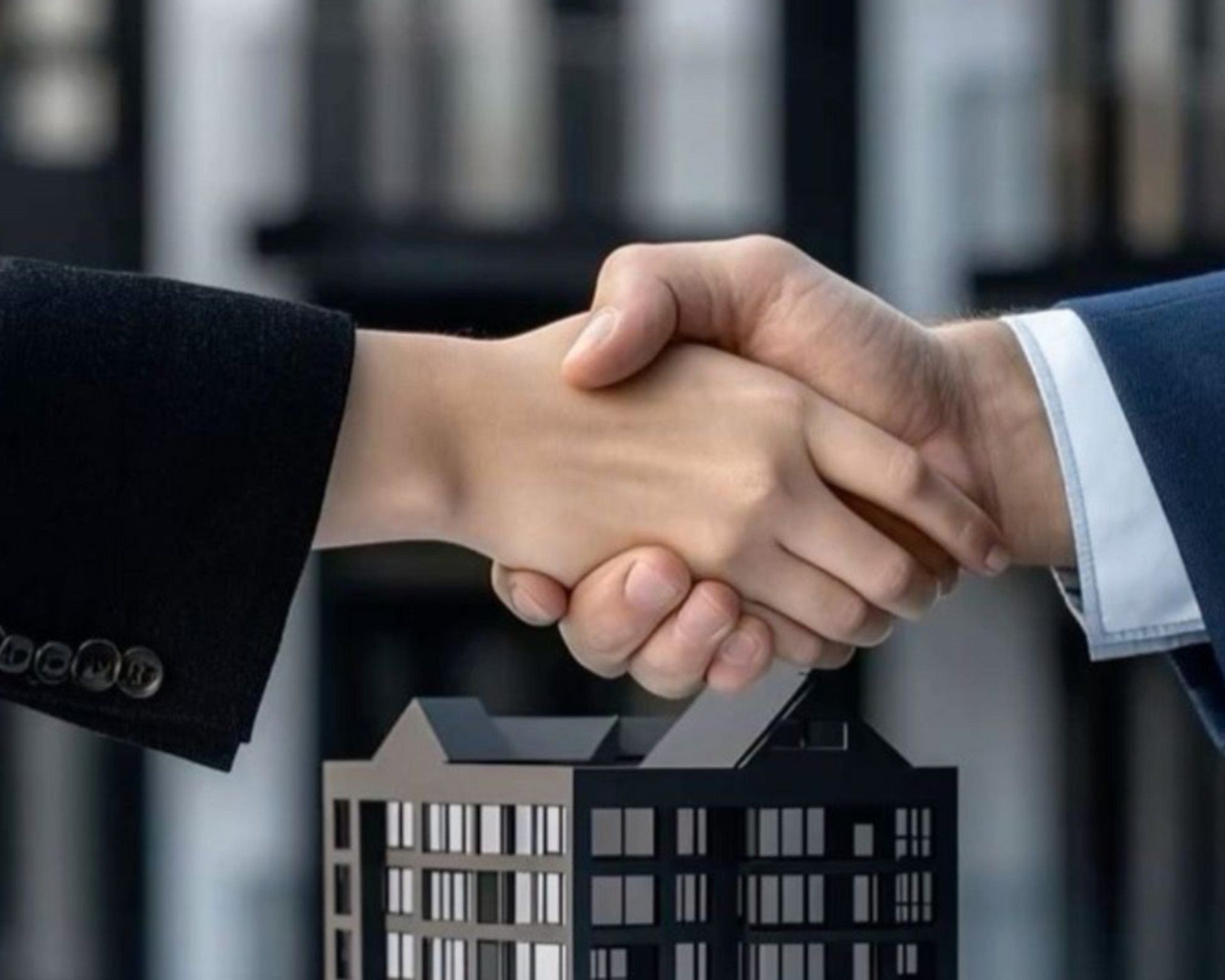 Handshake over a miniature building, symbolizing a real estate deal.
