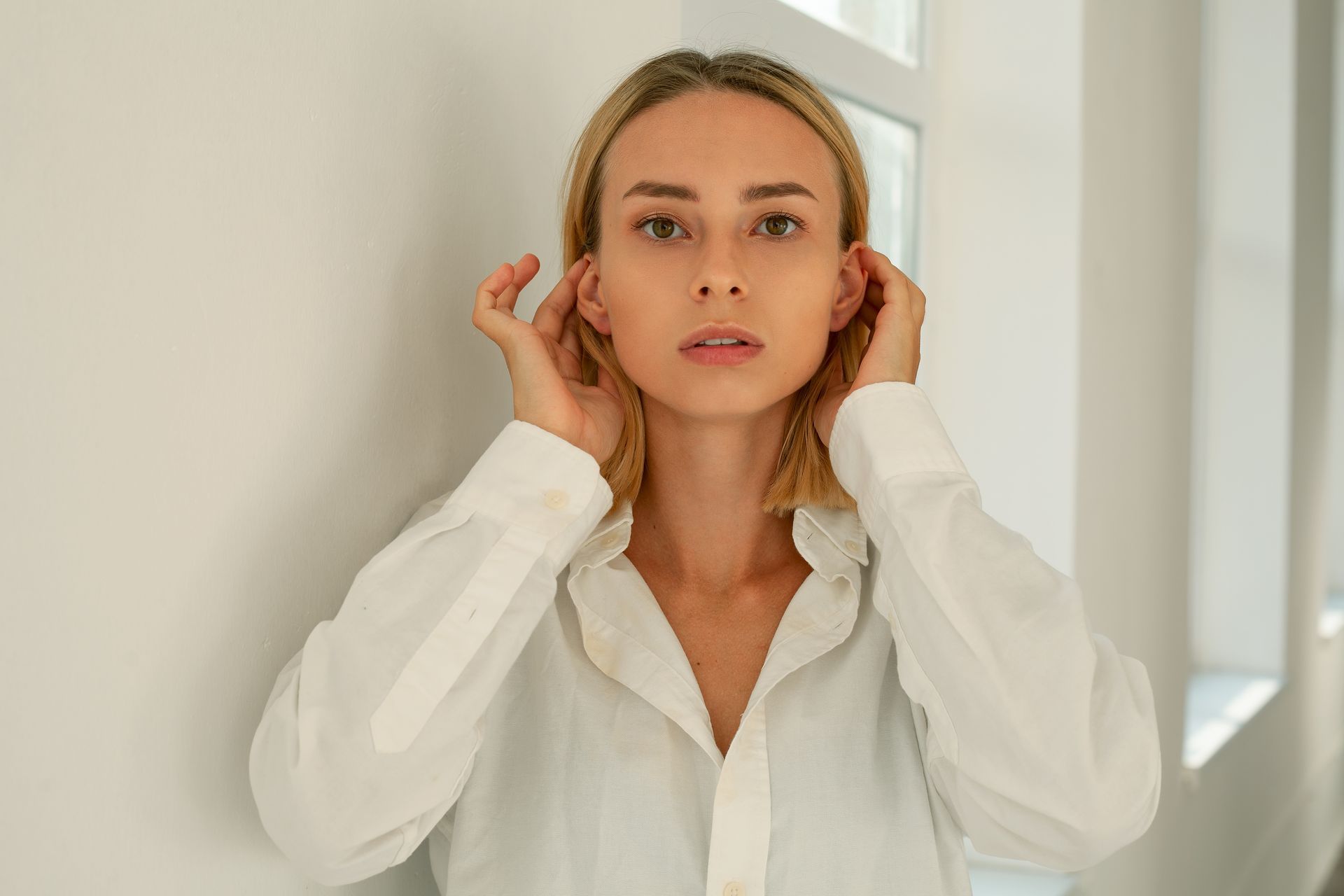 A woman in a white shirt is covering her ears with her hands.